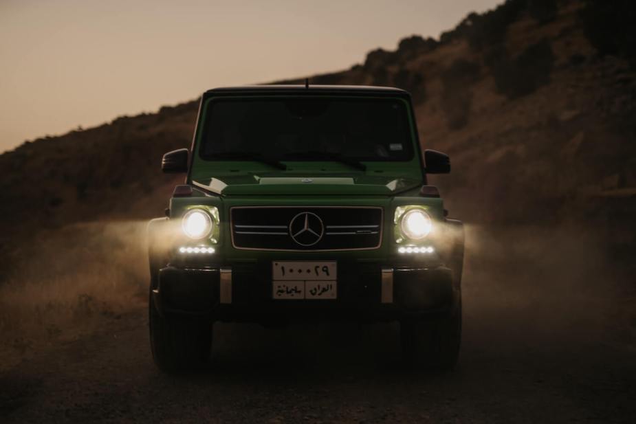 The boxy shape of a Mercedes G Wagon SUV with its headlights on.