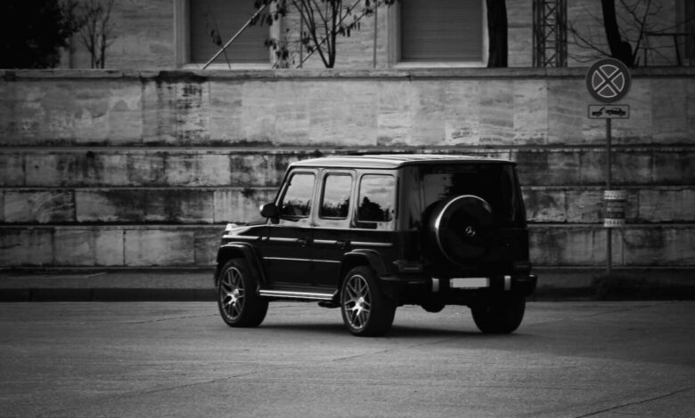 Black and white photo of a G-Class Wagon Mercedes SUV parked facing away from the camera, a brick wall visible in the background.