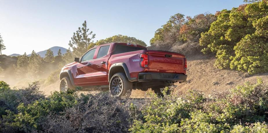 The back of a red 2023 Chevrolet Colorado pickup truck is parked in the dirt 