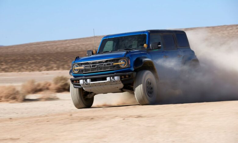A blue 2022 Ford Bronco Raptor undergoing off-road driving training through dirt and sand