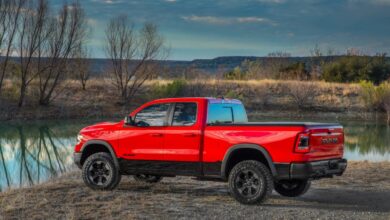 Promo photo of a bright red Ram 1500 with a cheap quad cab configuration parked by a lake.
