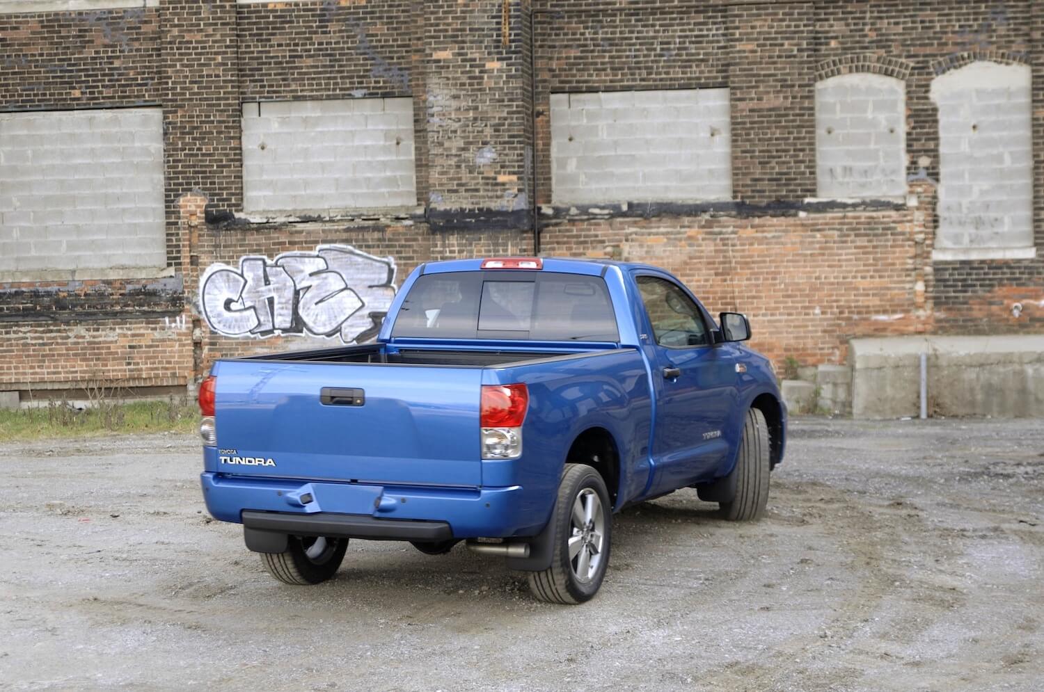 The back of a blue 2007 Toyota Tundra parked in front of a brick wall with graffiti. 