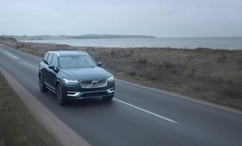 A Volvo XC90 Recharge luxury midsize SUV model in Denim Blue driving past the sea in a fog