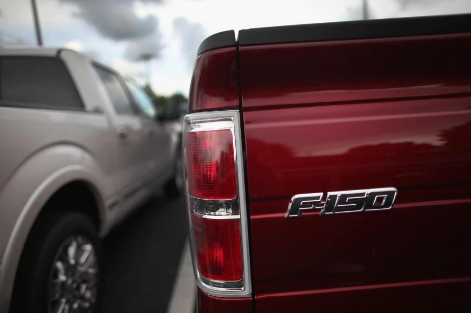 Red tailgate of a red Ford F-150 parked at dealership, silver pickup truck visible in the background.