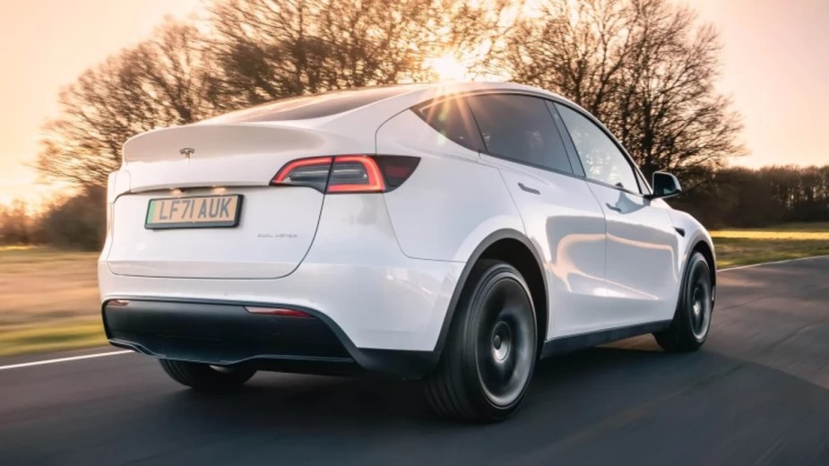Rear view of a small white 2023 Tesla Model Y electric SUV with a sunset in the background.