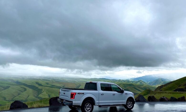 A white F-150 parked on a mountain road, a mountain range and dark clouds visible in the background.