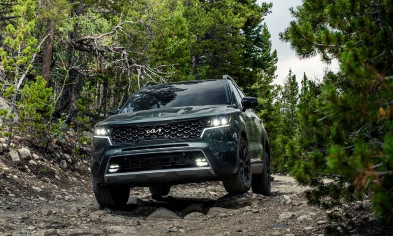 A dark green 2023 Kia Sorento X-Line compact SUV model driving on a gravel dirt road in a forest