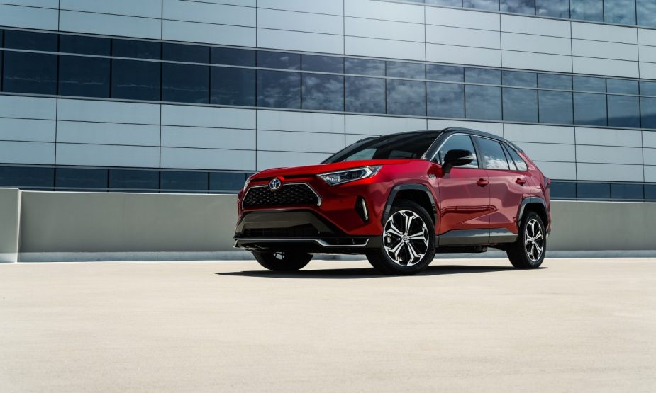 A red 2023 RAV4 Prime sits atop a garage near a large glass building. 