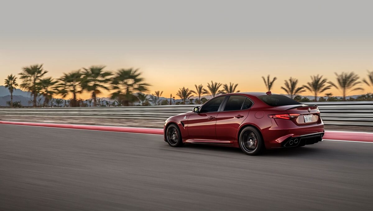 Like the Dodge Charger Hellcat, the red 2022 Alfa Romeo Giulia Quadrifoglio uses big horsepower to attack a sunset test track.