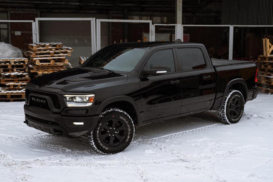 A black Ram 1500 pickup parked in front of a stack of pallets by the loading bay, in the snow.