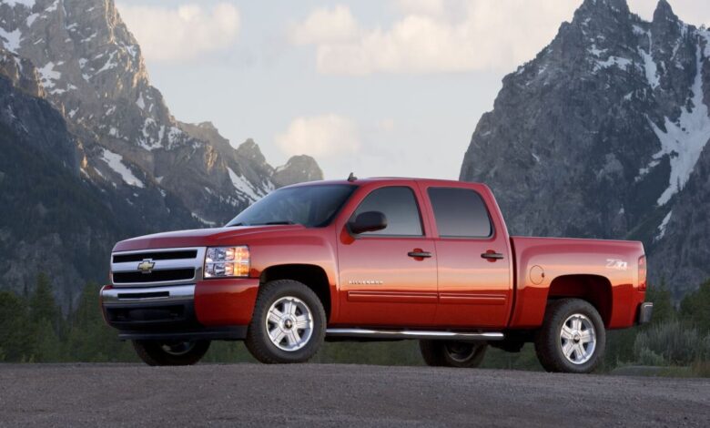 Promo photo of a red 2011 Chevrolet Silverado 1500 pickup truck parked in front of snow-capped mountains.