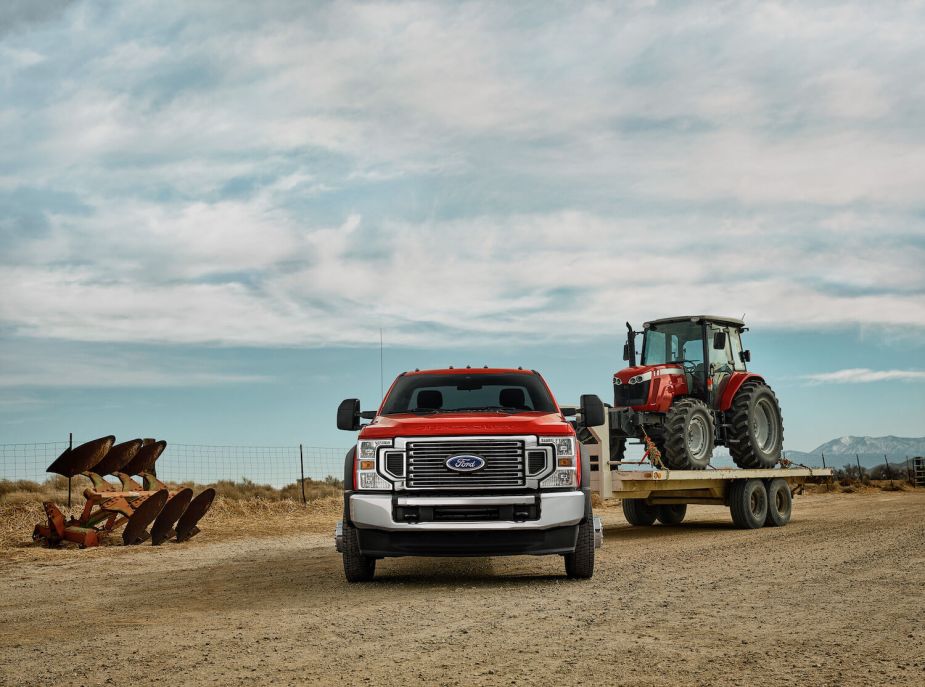 A red Super Duty pickup truck pulls a red farm tractor, a grazing field visible in the background.