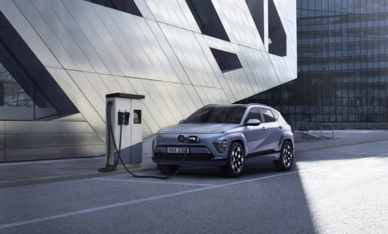 A new 2024 Hyunda Kona Electric plugged into a charging station in an urban landscape.