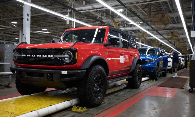 Red Ford Bronco rolls down an assembly line ahead of a blue Ford Ranger.