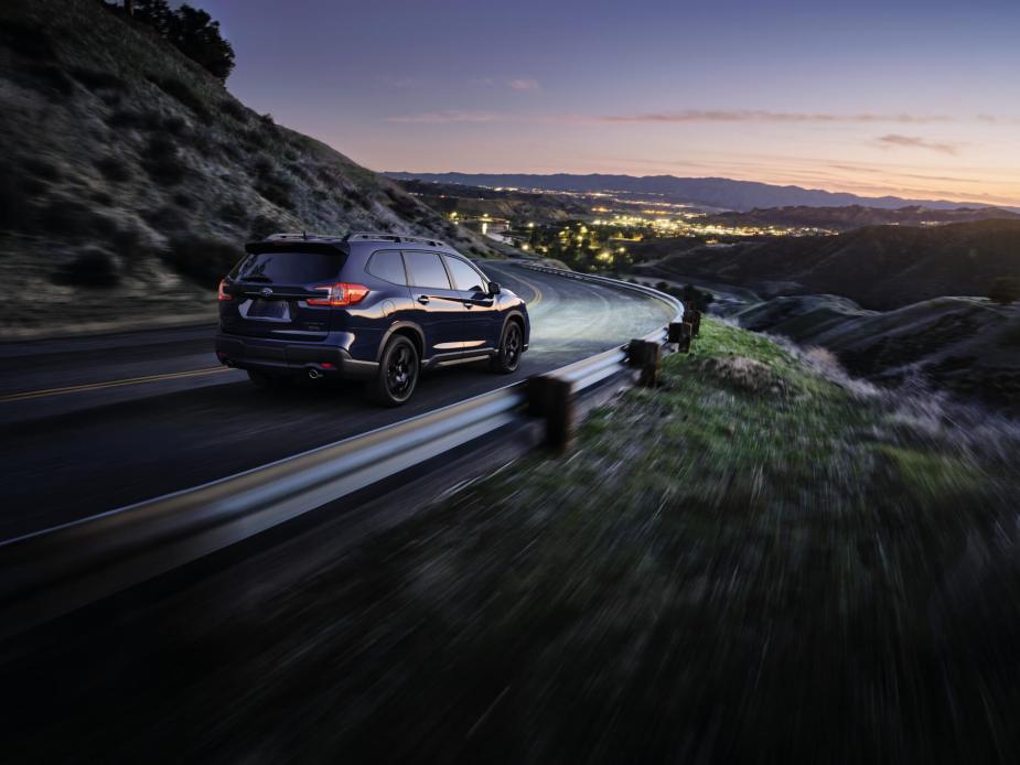 Rear view of a 2023 Subaru Ascent driving down a mountain road at sunset. 