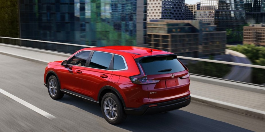 A small red 2023 Honda CR-V SUV is driving on the road. 