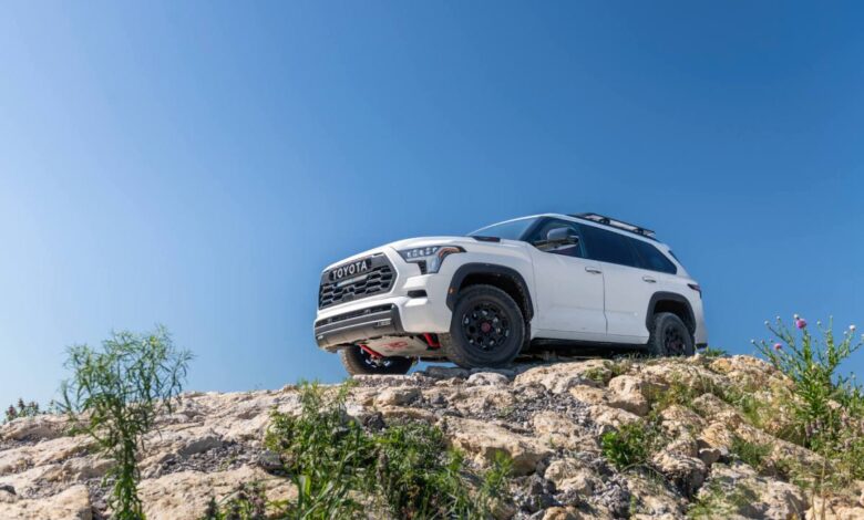A white 2023 Sequoia drives on a rocky trail - view from below looking up with blue sky in background.