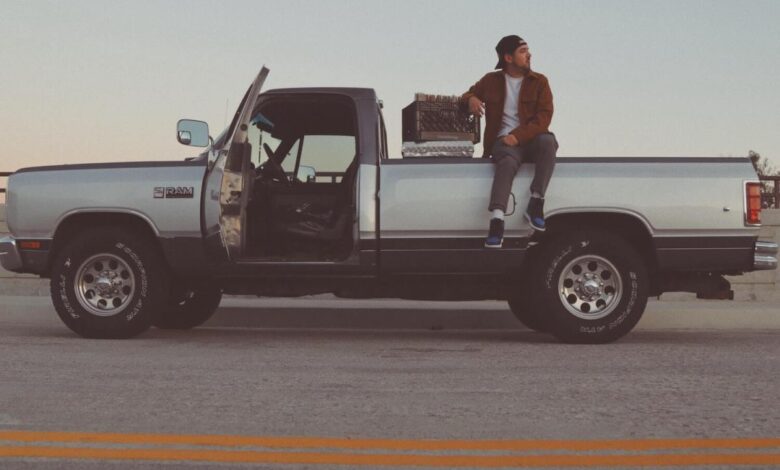 A man sits on the bed of his regular cab Dodge Ram pickup truck.