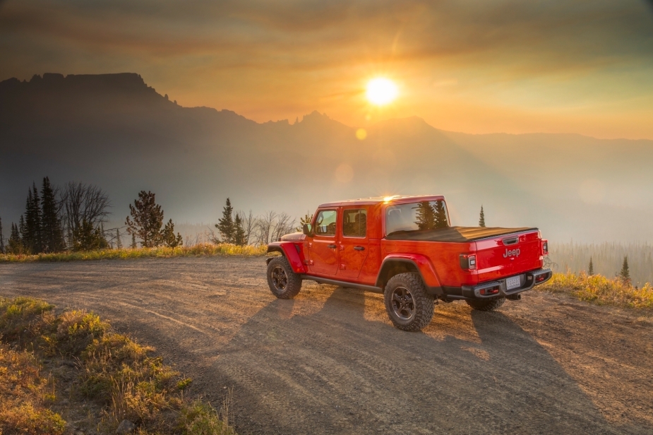 Red Jeep Gladiator pickup truck parked on a mountain trail, sunset in the background.