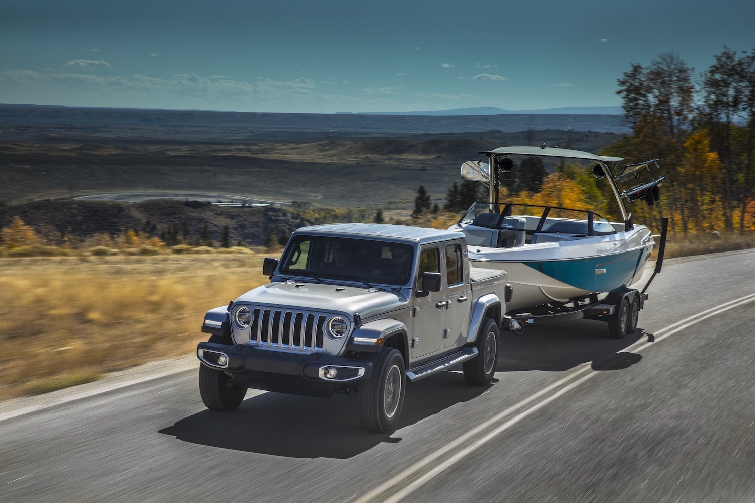A silver 2021 Jeep Gladiator pickup truck pulls a rowboat on a mountain road to show off the Ram 1500's capability levels.