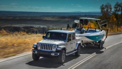 A silver 2021 Jeep Gladiator pickup truck tows a boat up a mountain road to show its Ram 1500 levels of capability.