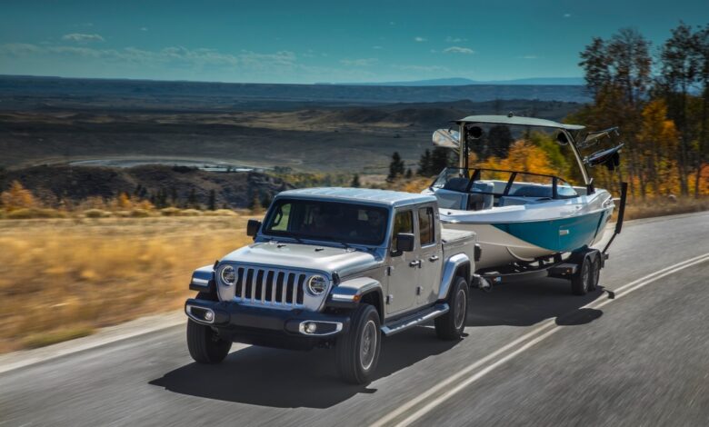 A silver 2021 Jeep Gladiator pickup truck tows a boat up a mountain road to show its Ram 1500 levels of capability.