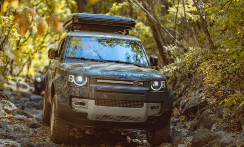Head-on view of a Land Rover Defender traversing a rocky and heavily wooded trail.