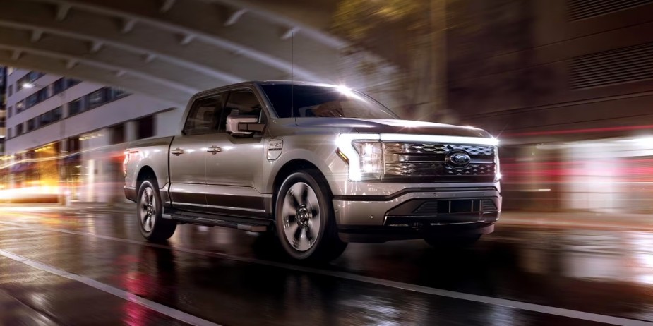 A gray 2023 Ford F-150 Lightning electric pickup truck is driving on the road. 