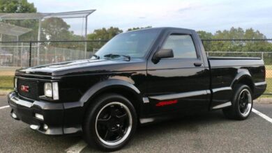 A black 1991 GMC Syclone supertruck parked in front of a fence for a promo shot.