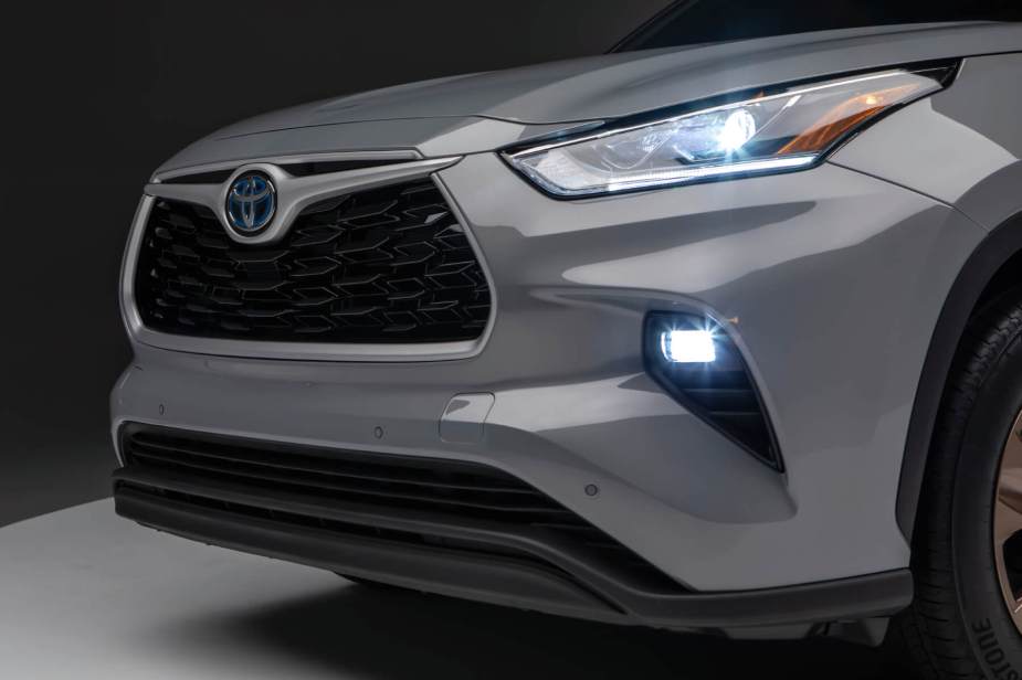 Diagonal front view of a gray 2023 Highlander Hybrid with headlights and fog lights on. 
