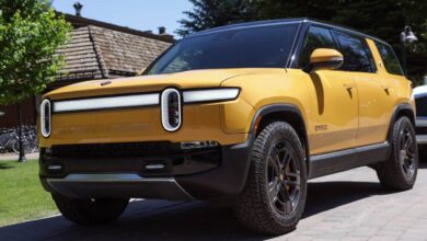 A yellow Rivian R1S electric SUV sits in front a green lawn under midday sun.