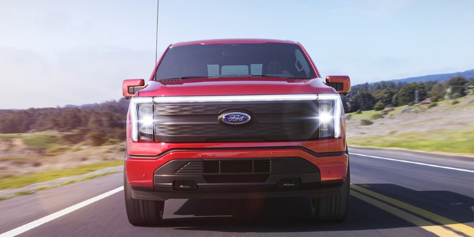 A red Ford F-150 Lightning electric pickup truck drives down the road.